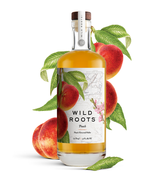 Bottle of Wild Roots Peach vodka with peaches and leaves on a white background